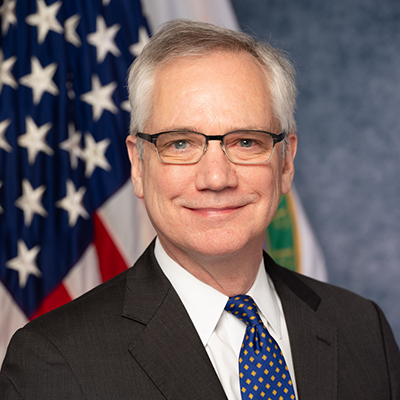 Andrew Light, a white man who wears glasses and stands in front of an American flag.