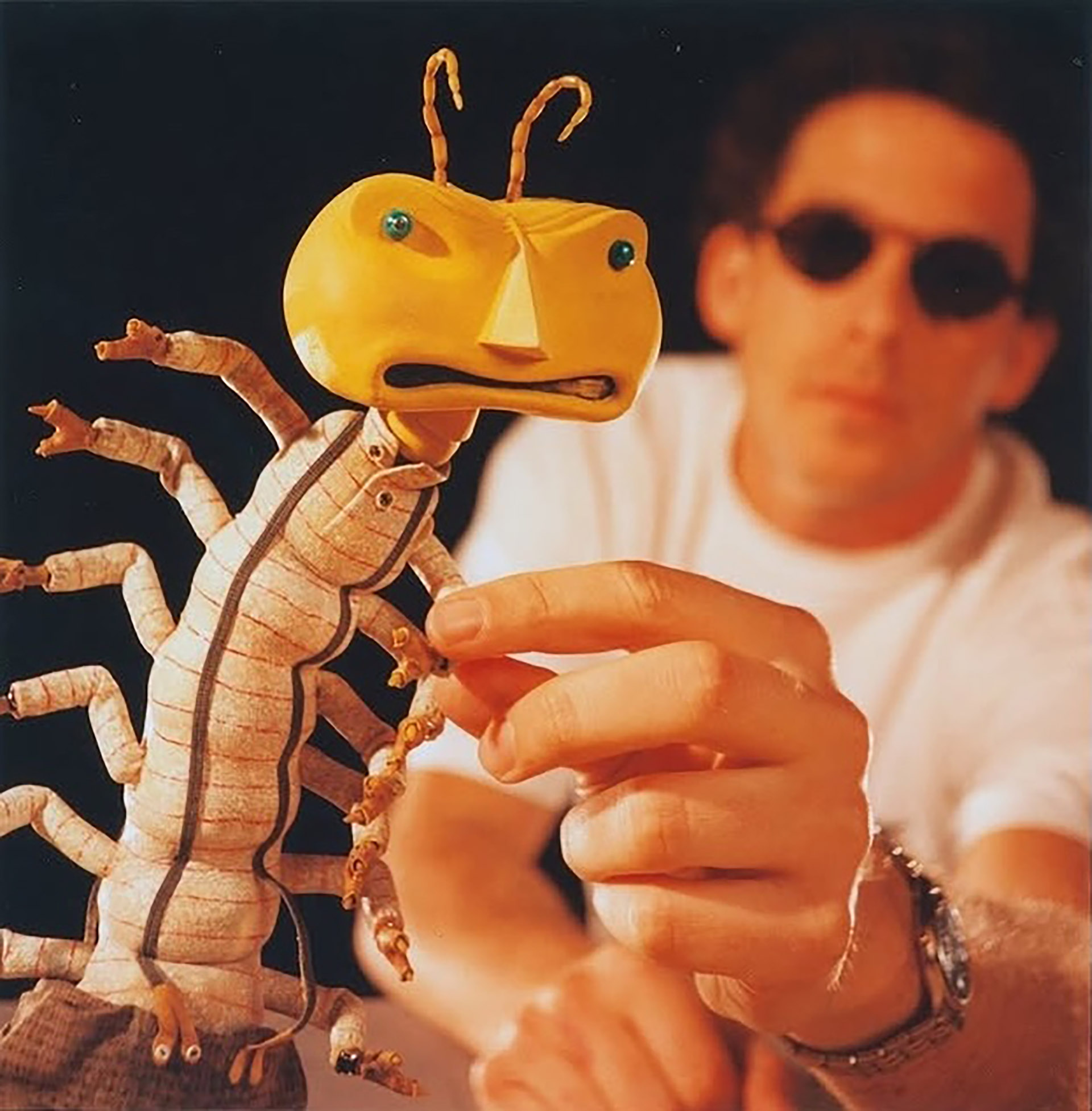 Artist Rich Zim holds a claymation model with a yellow head and segmented limbs.